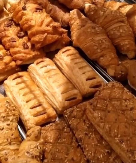 Assortimento di pasticcini e croissant dorati impilati uno sull'altro in una vetrina di una pasticceria.
