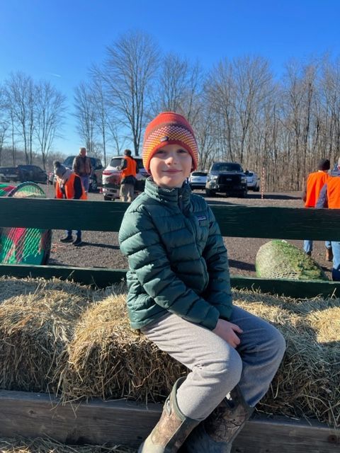 A young boy is sitting on a bale of hay.