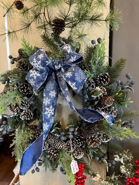 A christmas wreath with pine cones , berries , and a blue bow.
