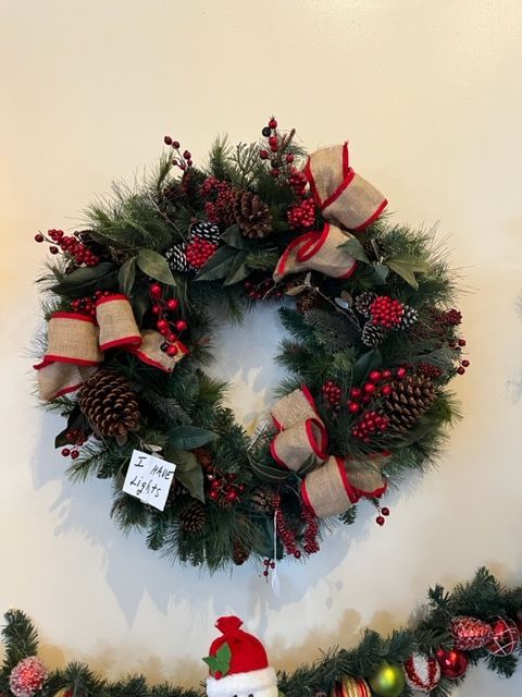 A christmas wreath with red berries and pine cones is hanging on a wall.