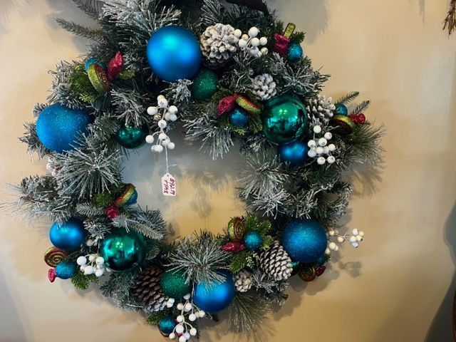 A christmas wreath with blue and green decorations is hanging on a wall.
