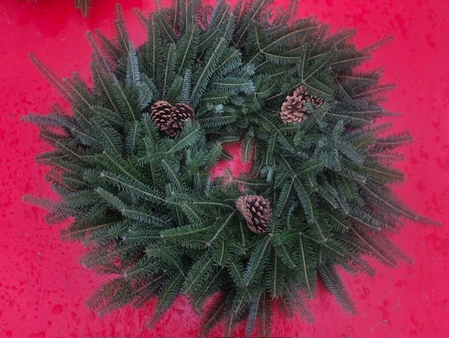 A christmas wreath with pine cones on a red surface.