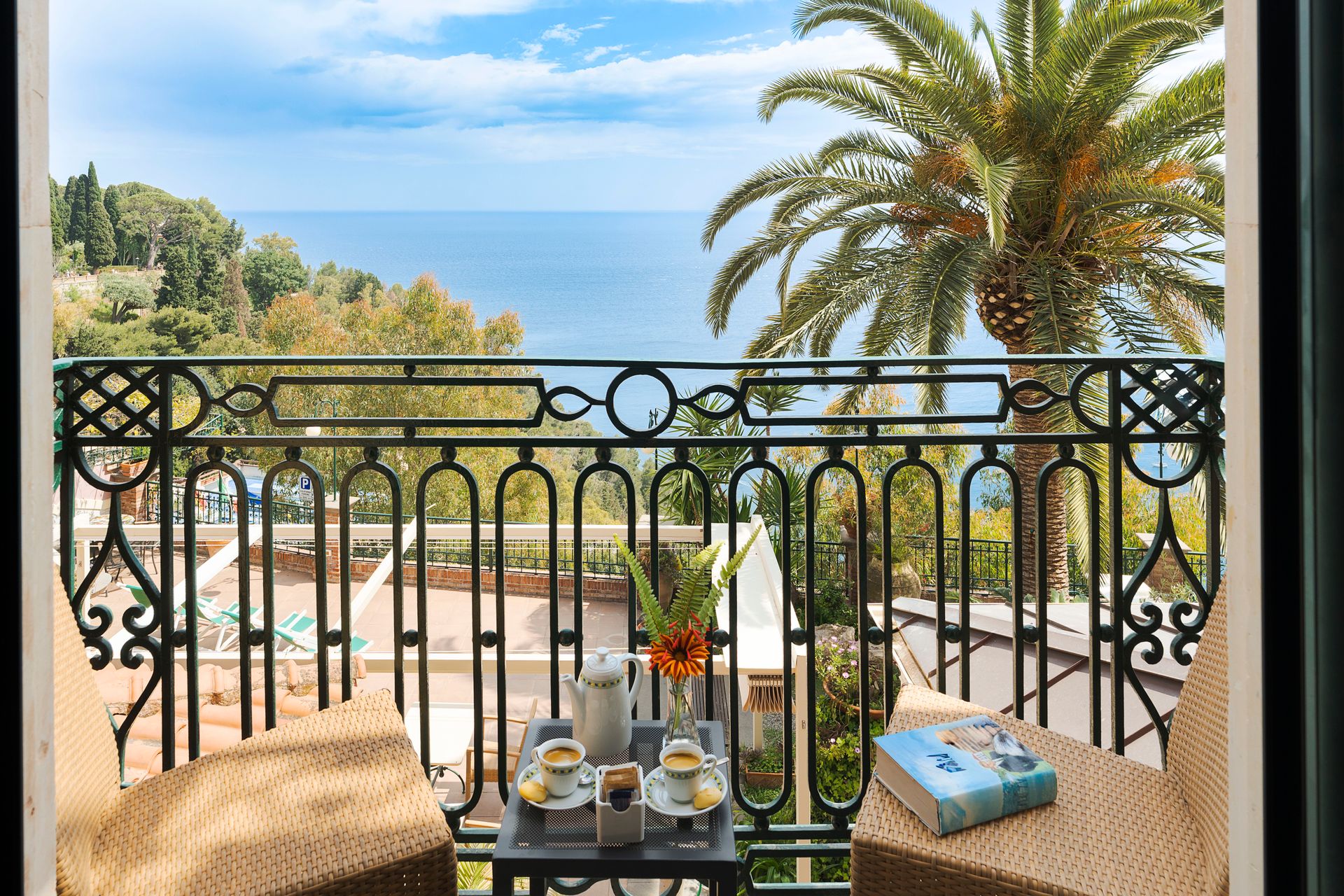 Table de balcon avec café donnant sur une piscine ensoleillée en bord de mer et des palmiers