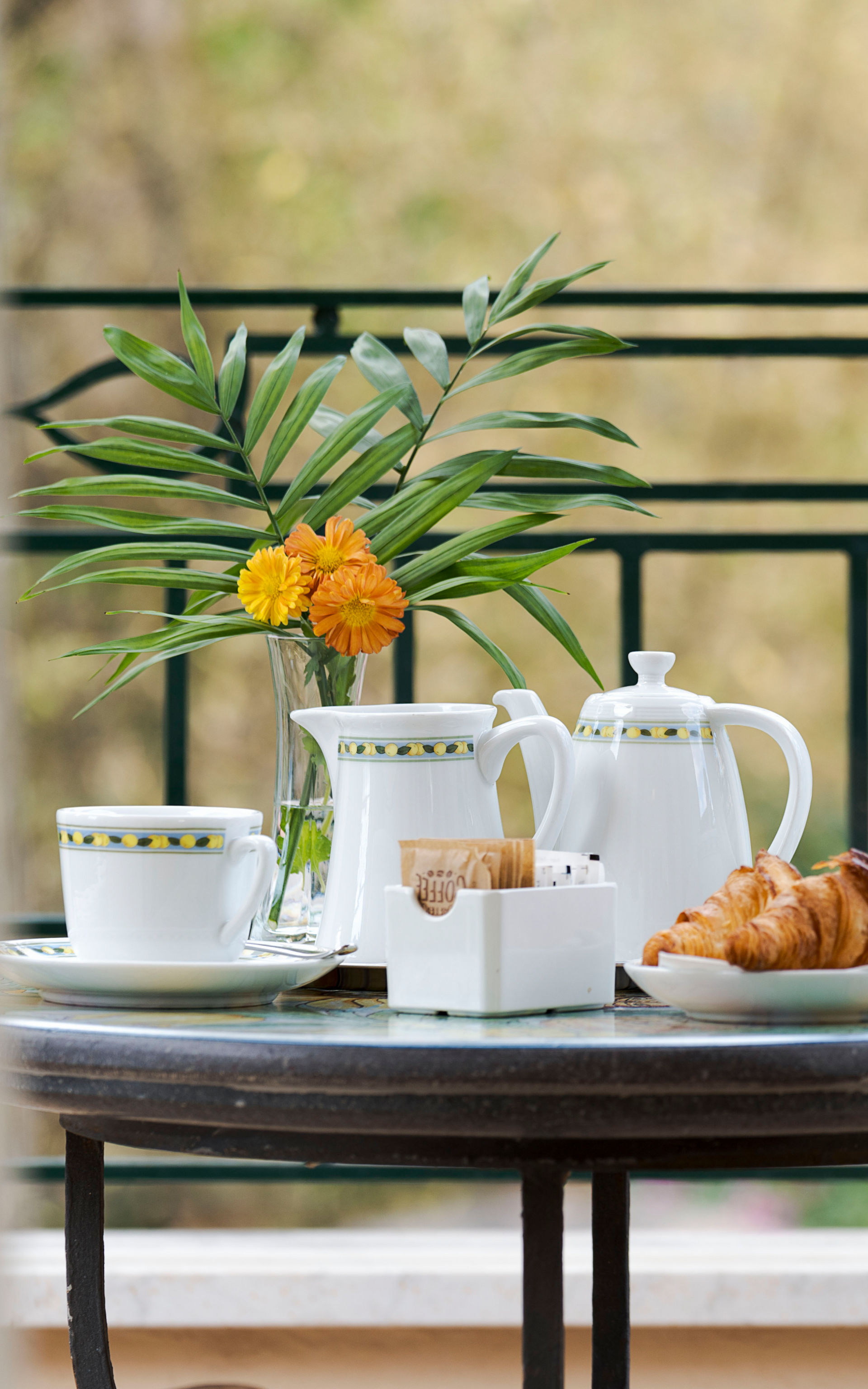 Service à thé avec théière blanche, tasses, croissant et fleurs jaunes sur une table à l'extérieur