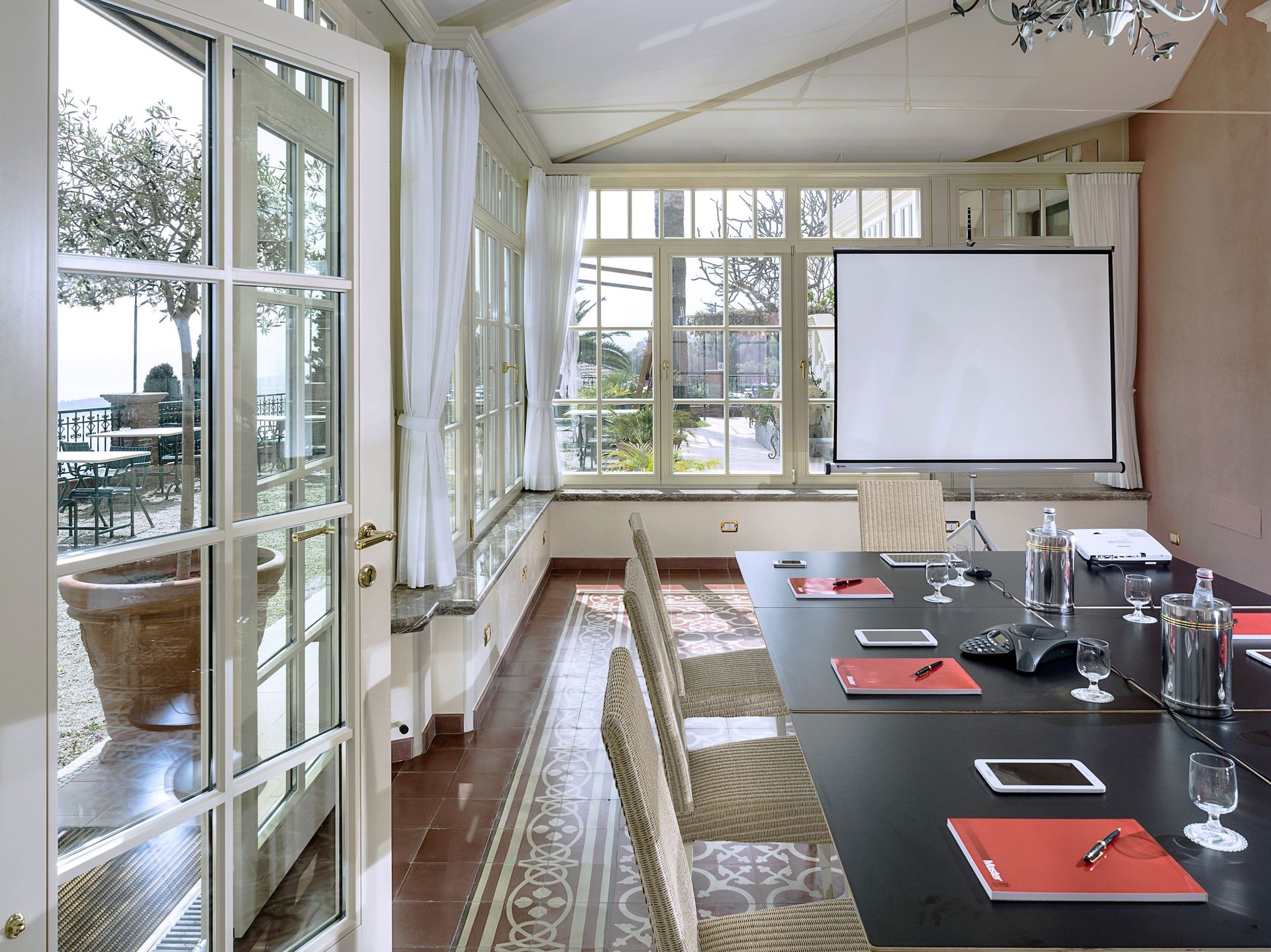 Bright conference room with table, chairs, projector screen, and large windows overlooking outdoors