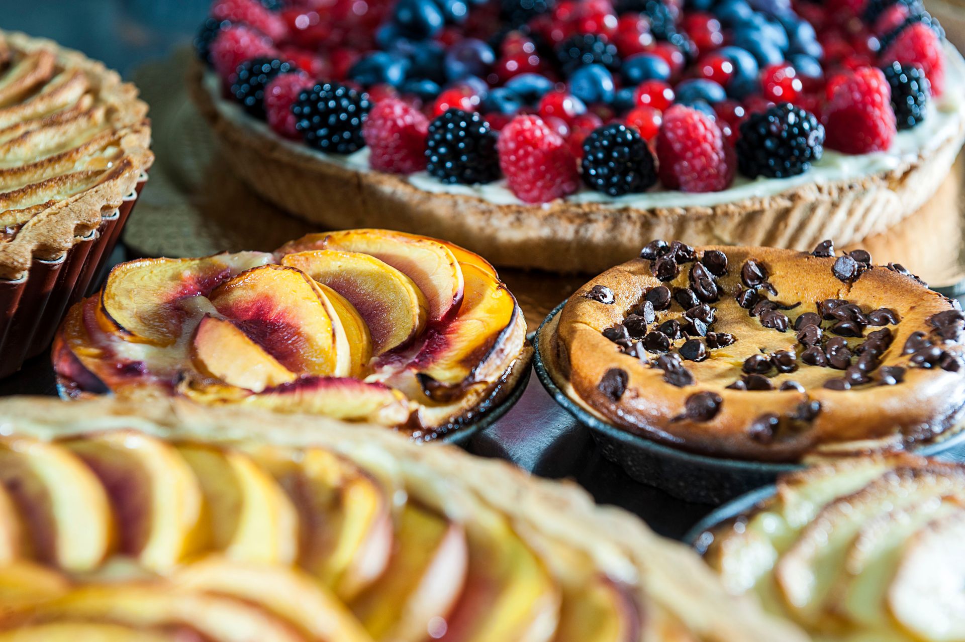 Su un tavolo, un assortimento di crostate di frutta e una crostata di frutti di bosco, guarnite con pesche