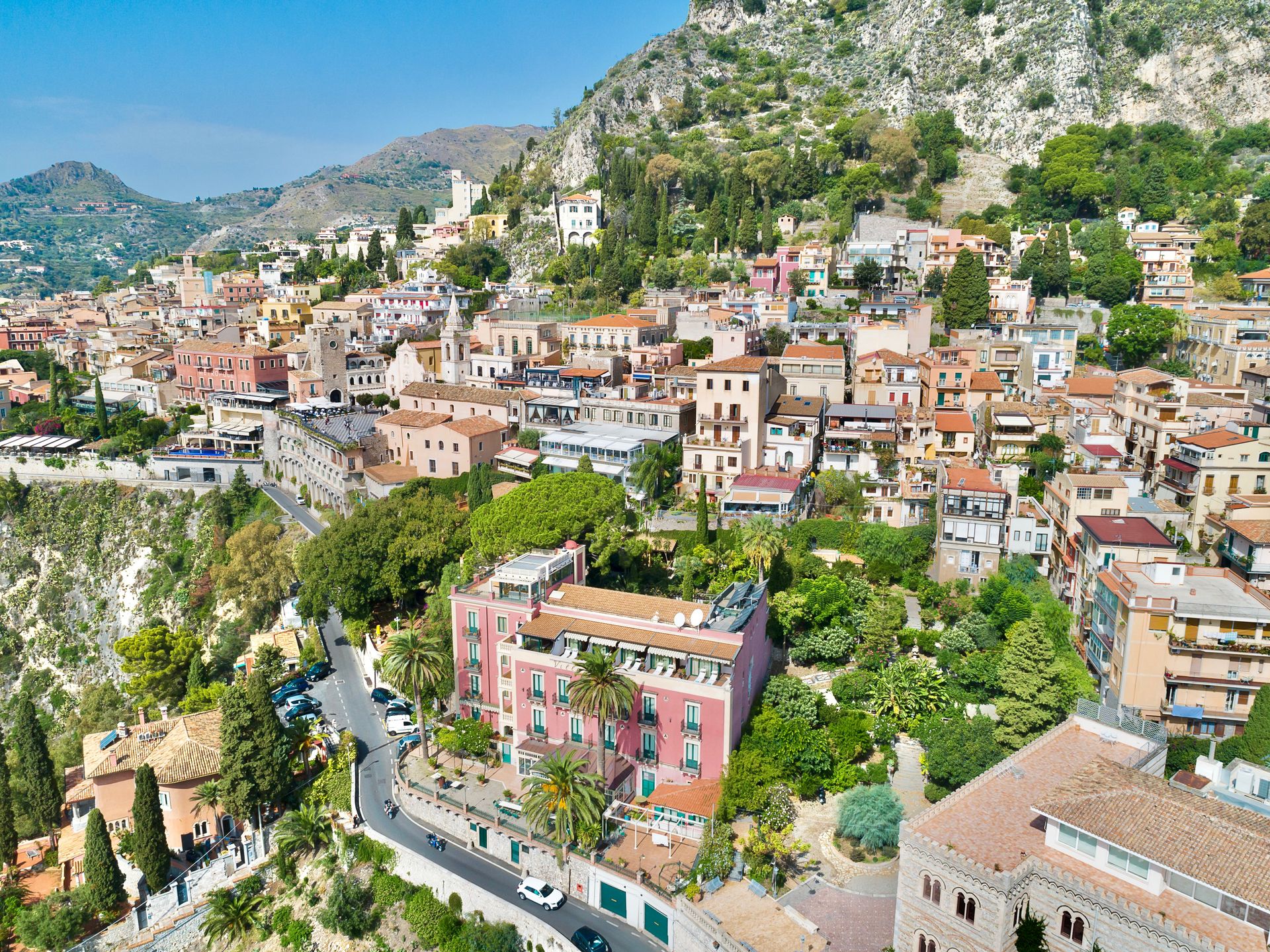 Pueblo en la ladera de una montaña con casas coloridas, caminos sinuosos y exuberante vegetación bajo una ladera rocosa.