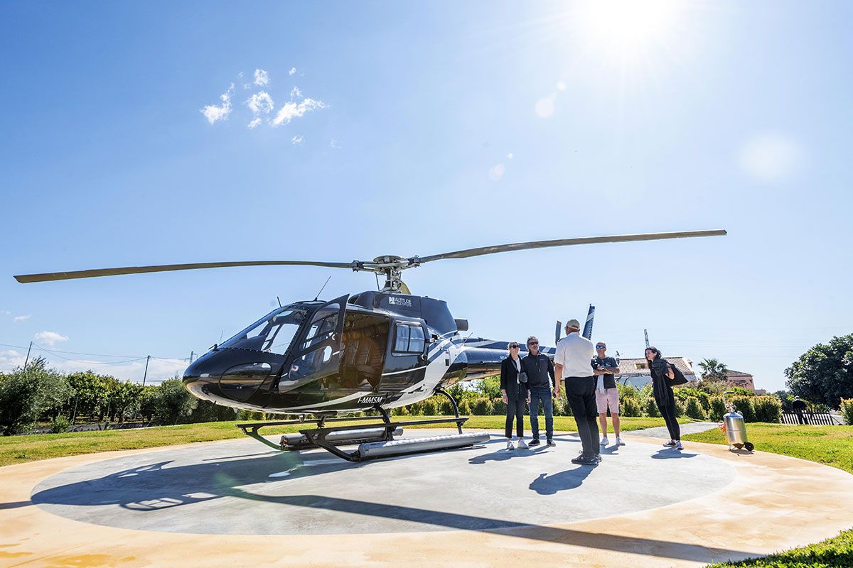 Black helicopter on a helipad with several people standing nearby under a bright blue sky