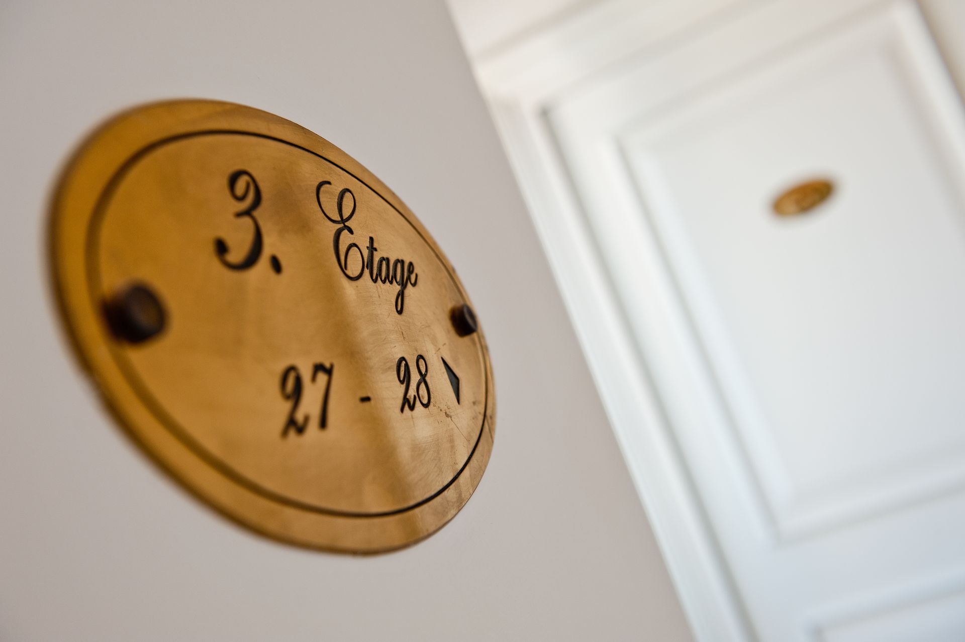 Enseigne ovale sur une porte indiquant « 3. Boutique 27-28 » en lettres noires sur plaque dorée