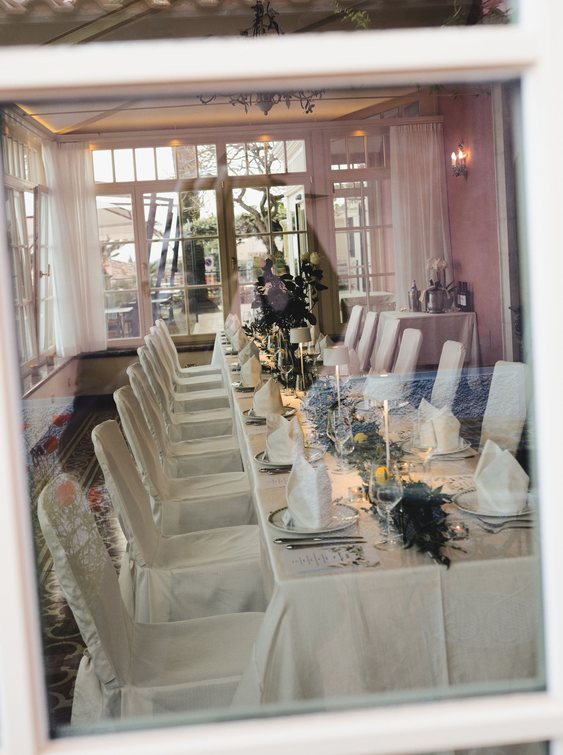 Elegant dining table set for a formal event, with white chairs, candles, and floral centerpieces in a bright room