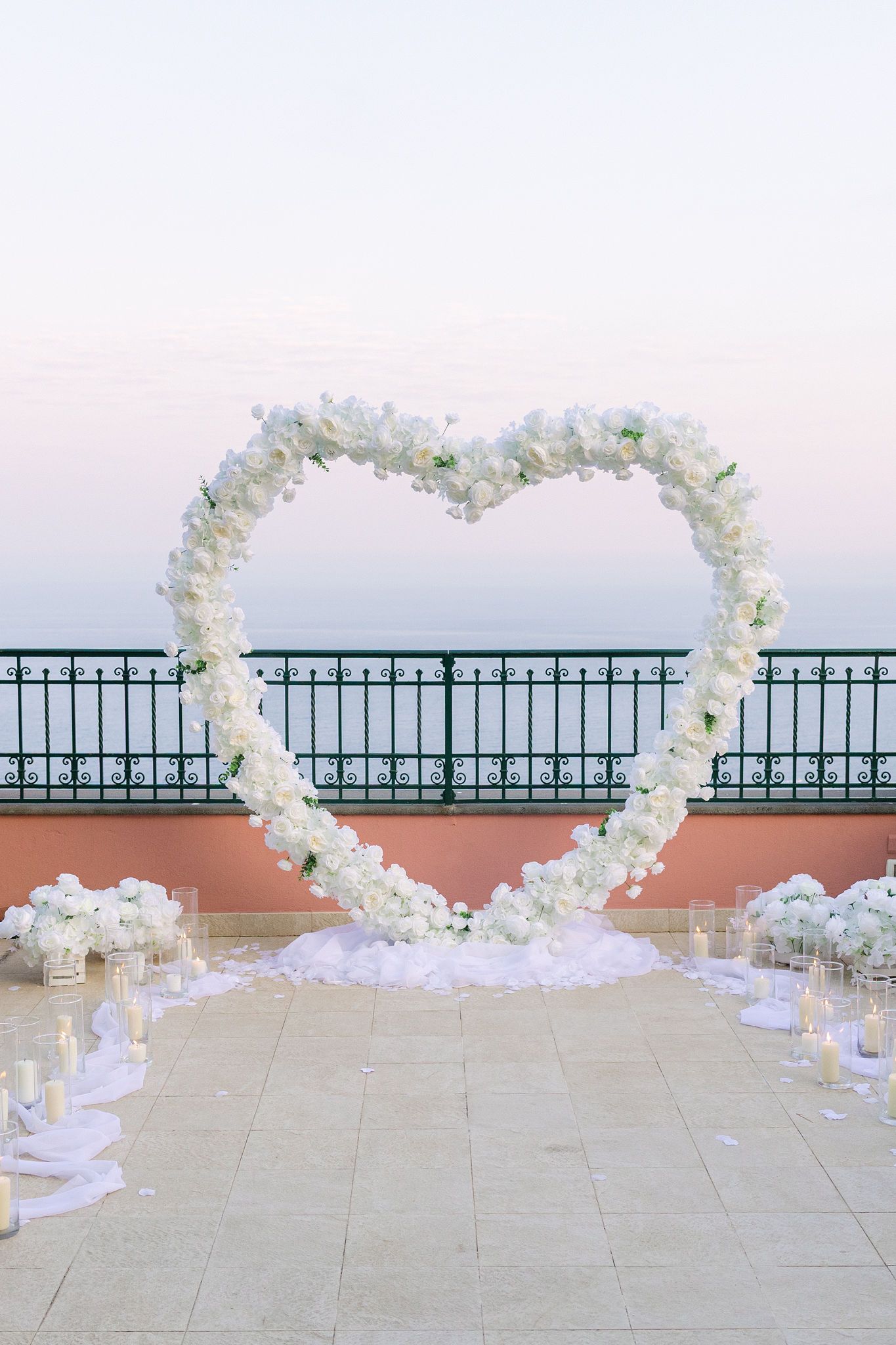 White floral heart arch at a seaside wedding aisle at sunset