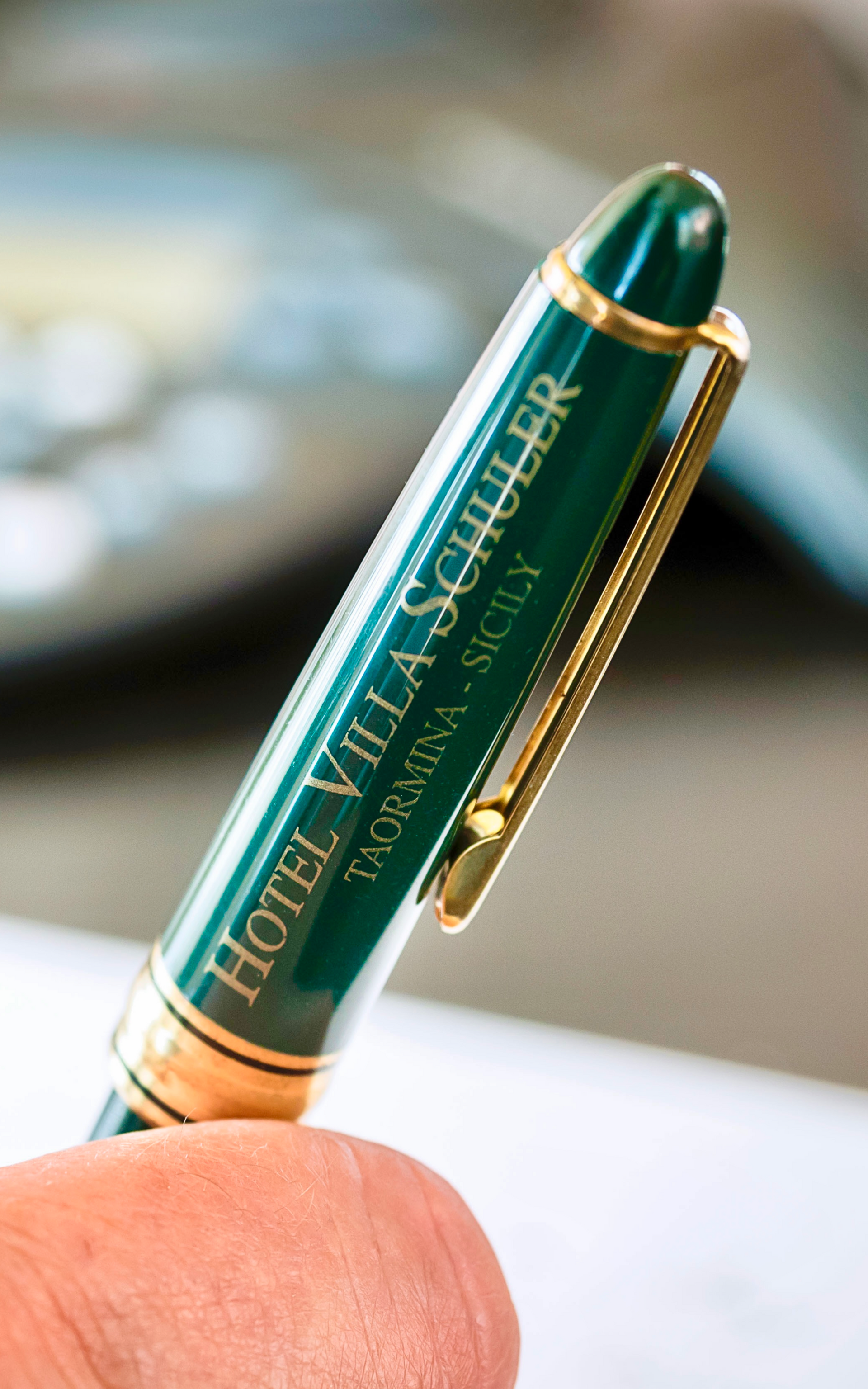 Green and gold pen clip with Hotel Schweizerhof Lucerne branding, held between fingers