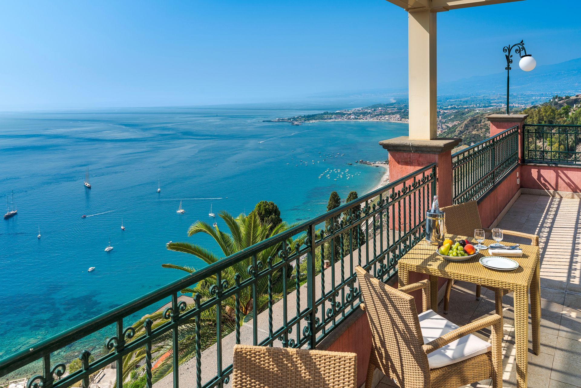Balkon mit Tisch und Stühlen mit Blick auf das strahlend blaue Meer und die Küstenstadt