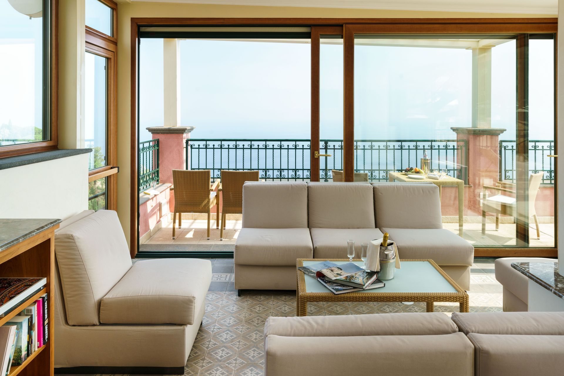 Modernes Wohnzimmer mit beigen Sofas, Couchtisch und großen Fenstern, die sich zu einem Balkon mit Meerblick öffnen.