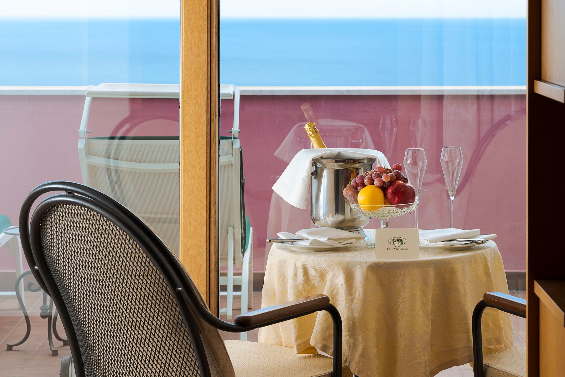 Balkon-Esstisch mit Obst, Stühlen und Meerblick hinter dem Glasgeländer