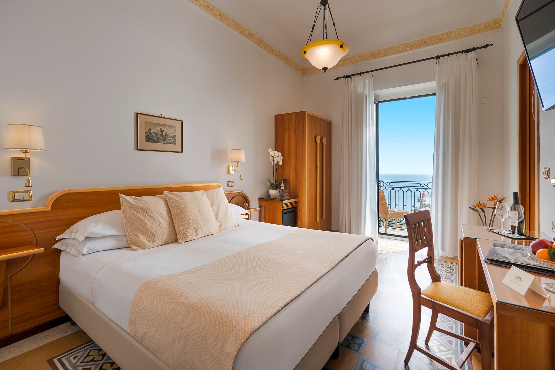 Helles Hotelzimmer mit großem Bett, Holzmöbeln und Balkon mit Meerblick.