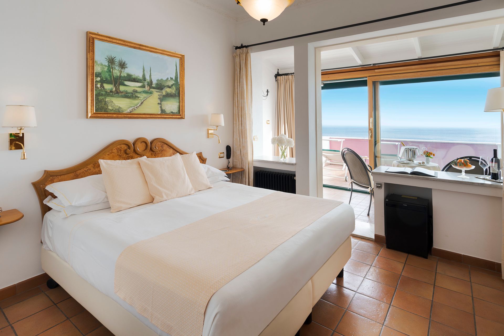 Helles Schlafzimmer mit geschnitztem Bett, Fliesenboden und Balkon mit Meerblick