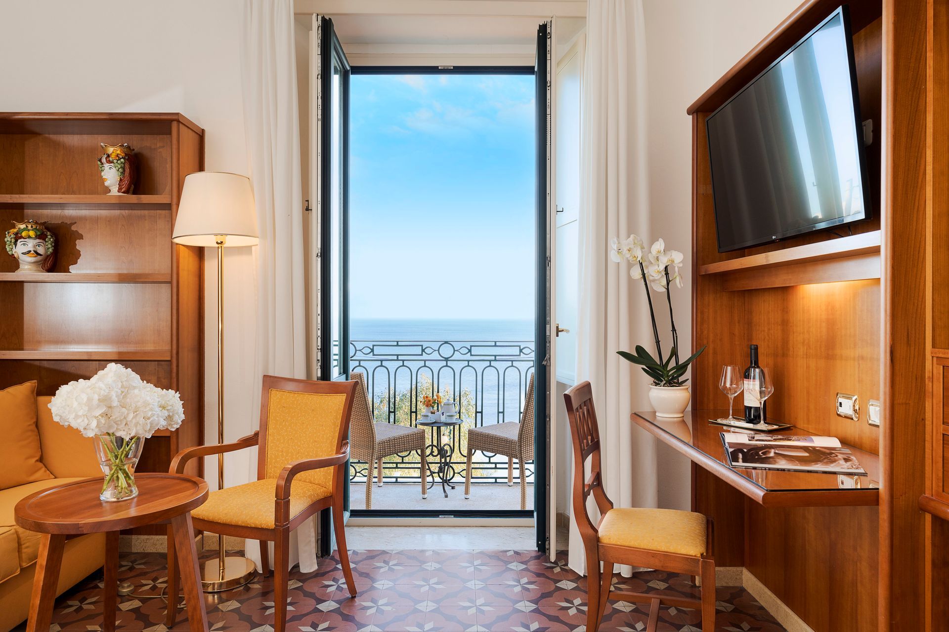 Luxuriöses Hotelzimmer mit Balkon und Meerblick, warmen Holzmöbeln und zwei Stühlen an einem Tisch