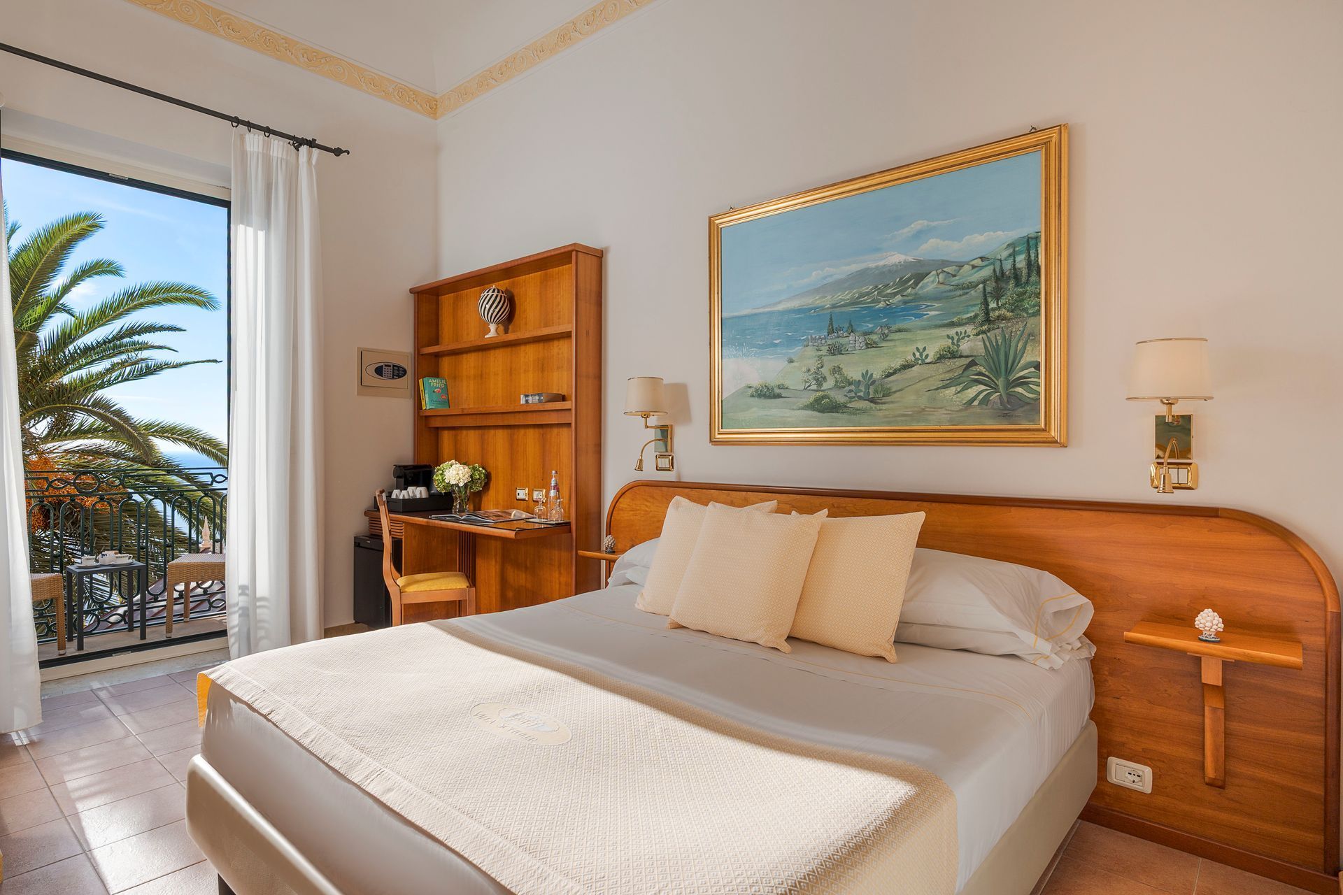 Chambre lumineuse avec lit, balcon avec vue et palmiers à l'extérieur de la fenêtre.