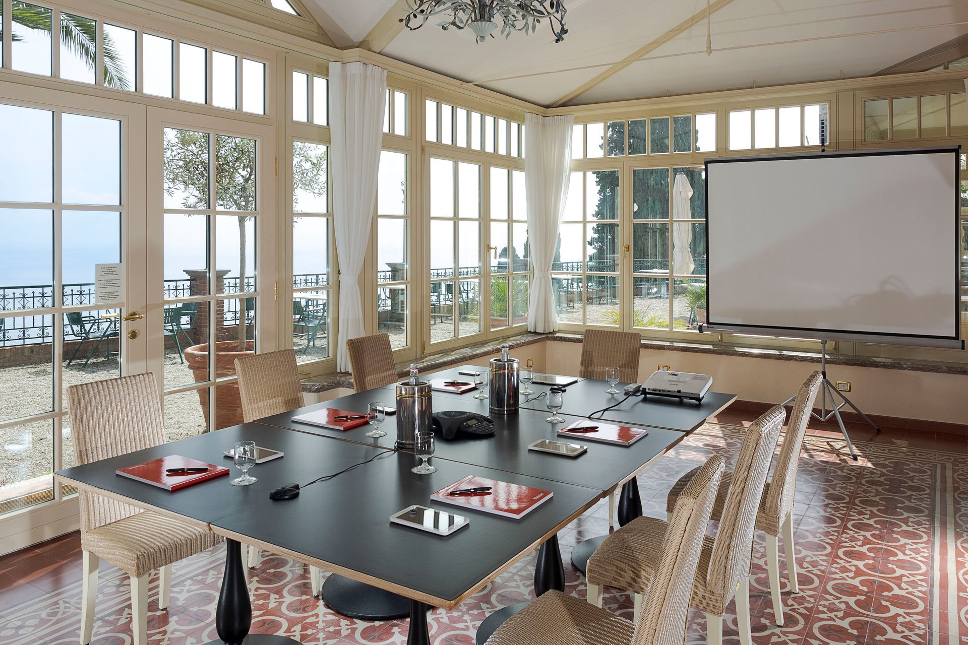 Sala de conferencias con una mesa larga, sillas, pantalla de proyector y grandes ventanales con vistas al agua.