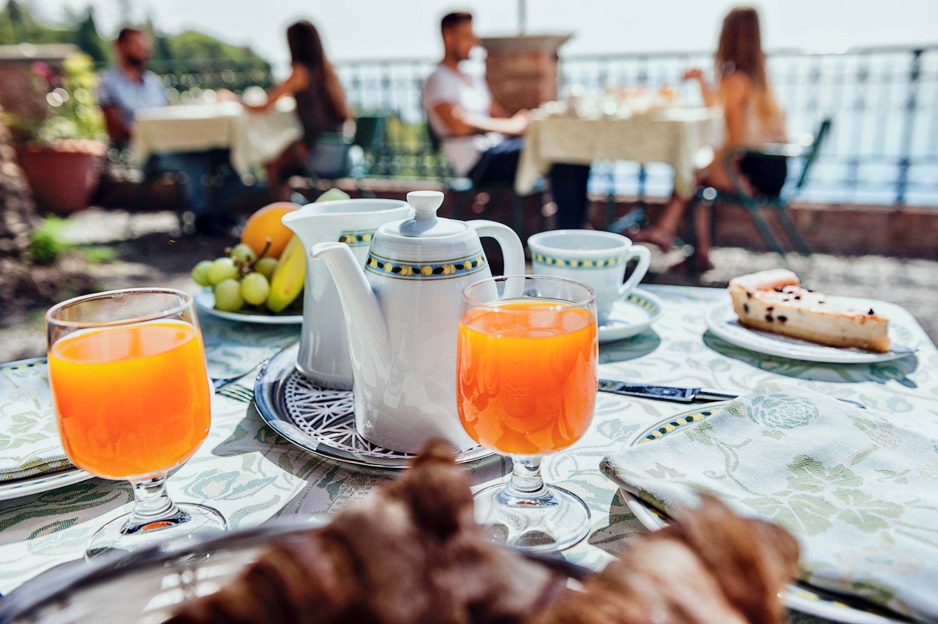 Frühstückstisch mit Orangensaft, Teekanne, Obstschale und Gebäck am Wasser
