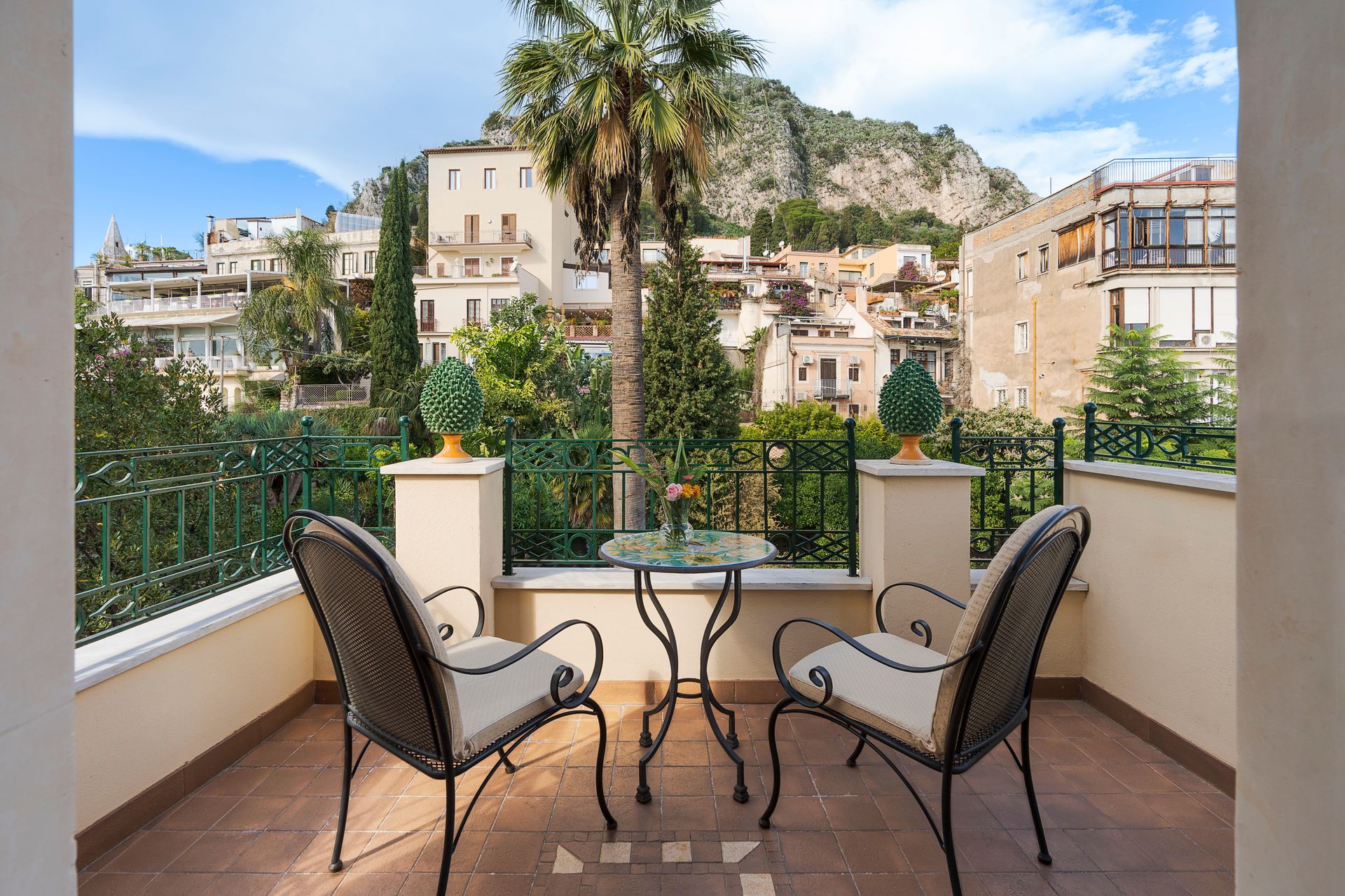 Zwei Korbstühle und ein Tisch auf einem Balkon mit Blick auf ein mediterranes Hügeldorf