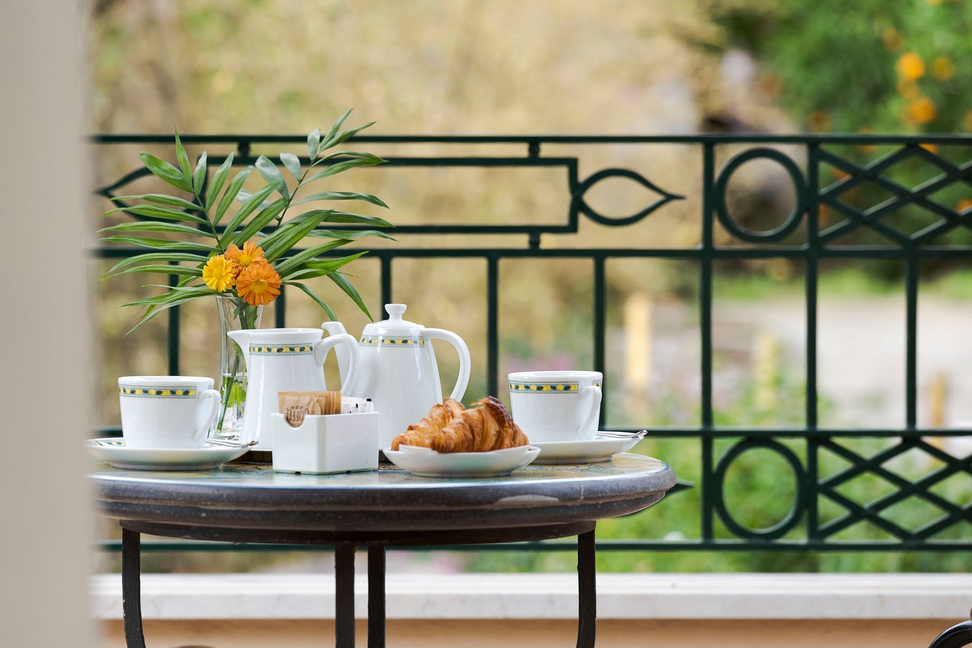Teeservice und Croissants auf einem Tisch mit einer Blumenvase auf einem Balkon