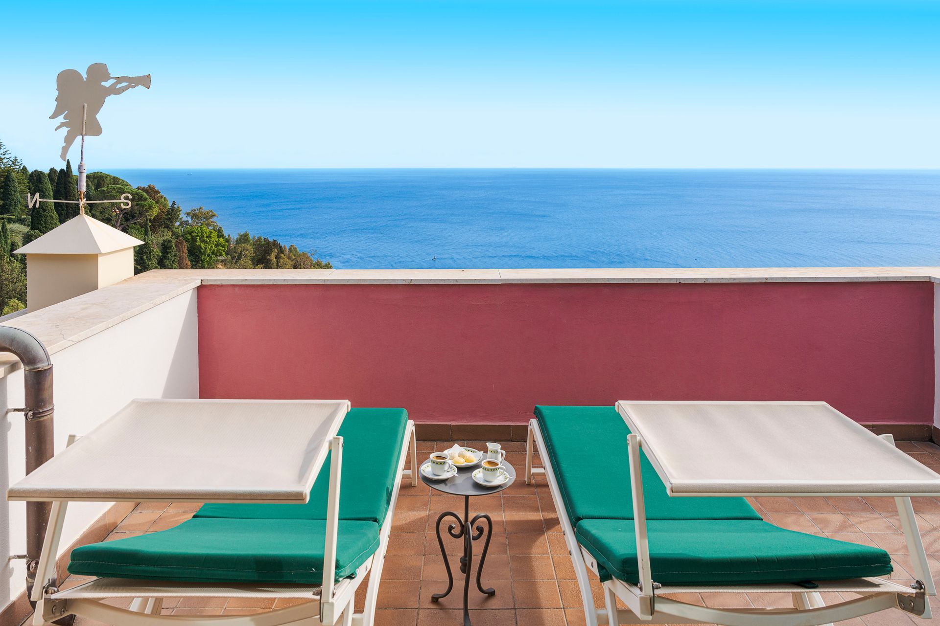 Terrasse direkt am Meer mit zwei grünen Liegestühlen, Tisch und einer rosafarbenen Wand mit Blick auf das Meer