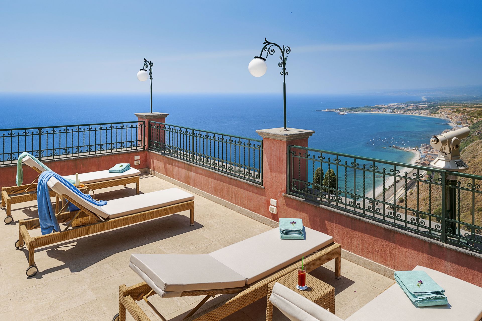 Terrasse mit Liegestühlen und Blick auf das blaue Meer und die Küste unter klarem Himmel