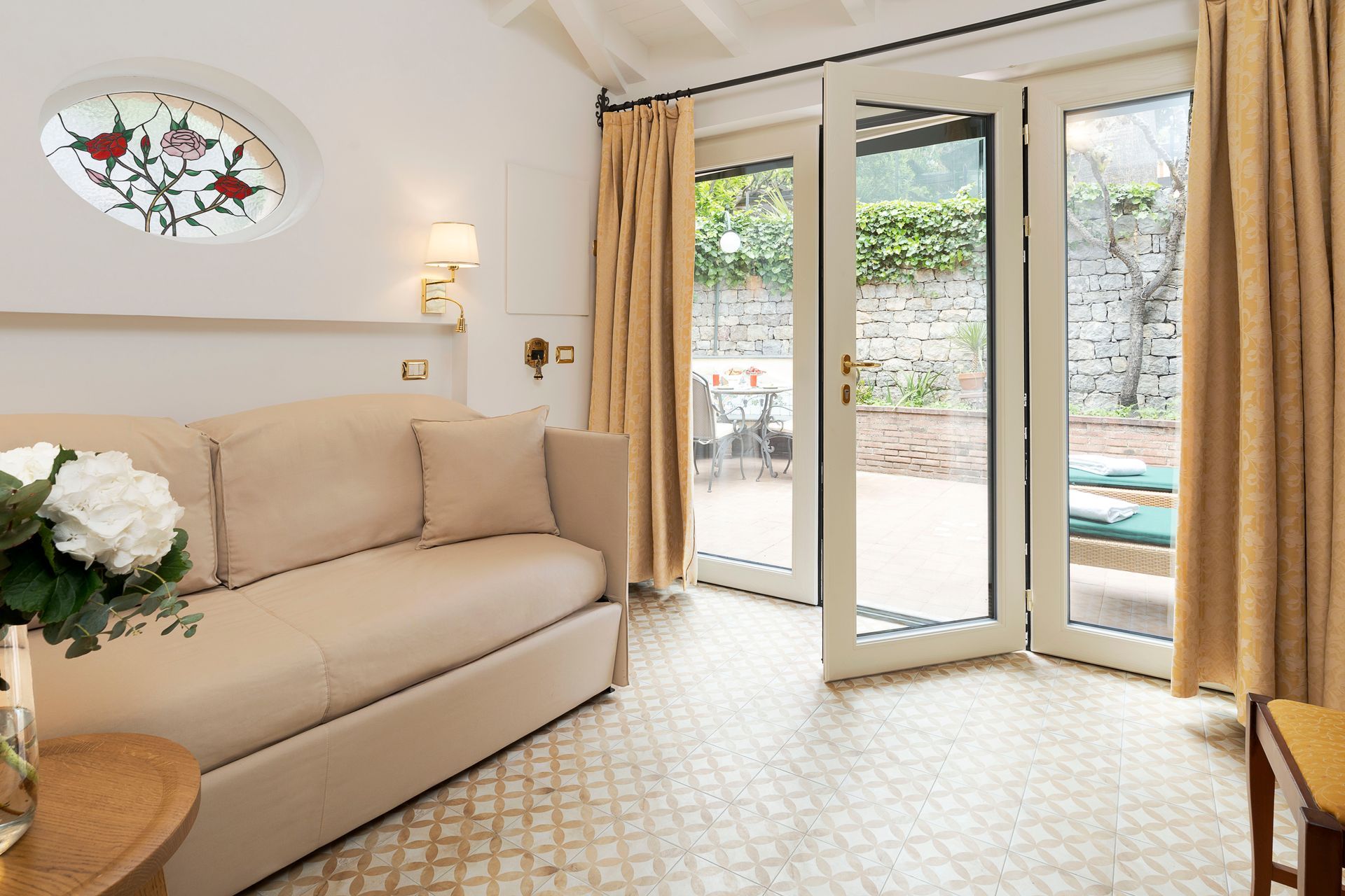Helles Wohnzimmer mit beigefarbenem Sofa, Blumen und offenen Glastüren zu einer Terrasse und einem Pool.