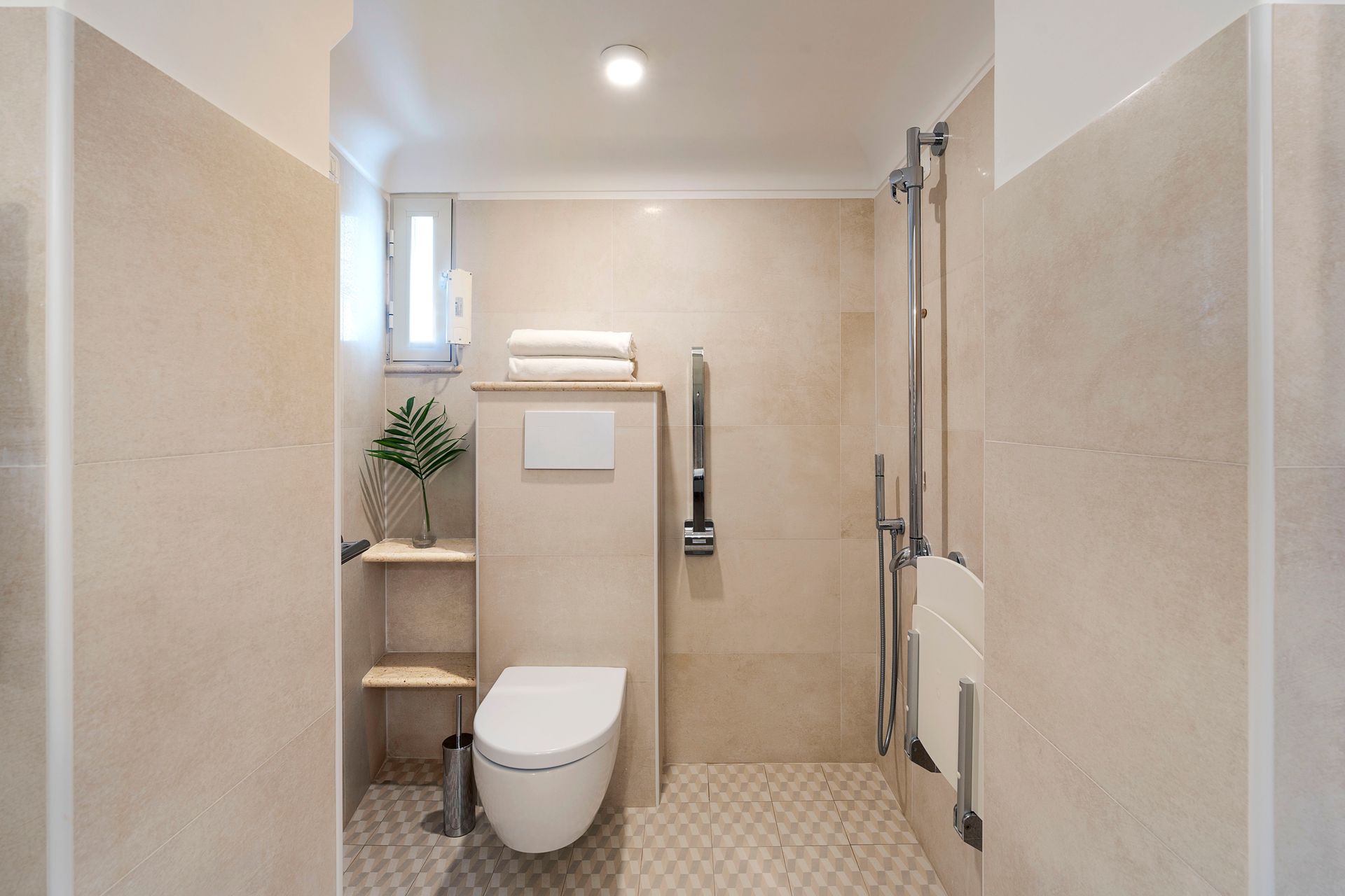 Barrierefreies, beige gefliestes Badezimmer mit Toilette, Haltegriff und ebenerdiger Dusche.