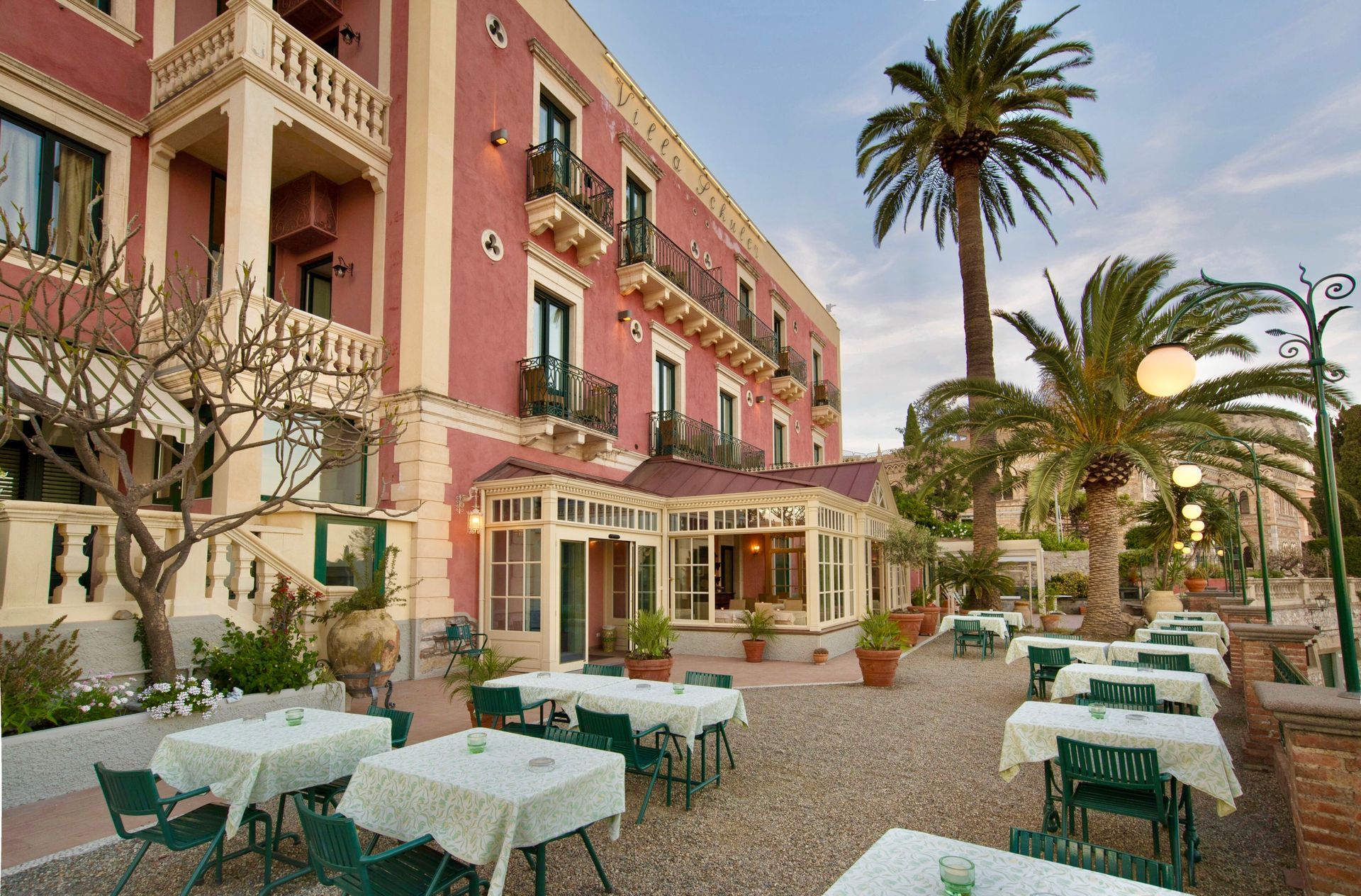 Rosafarbener Hotelinnenhof mit Palmen und Tischen und Stühlen für ein Café im Freien