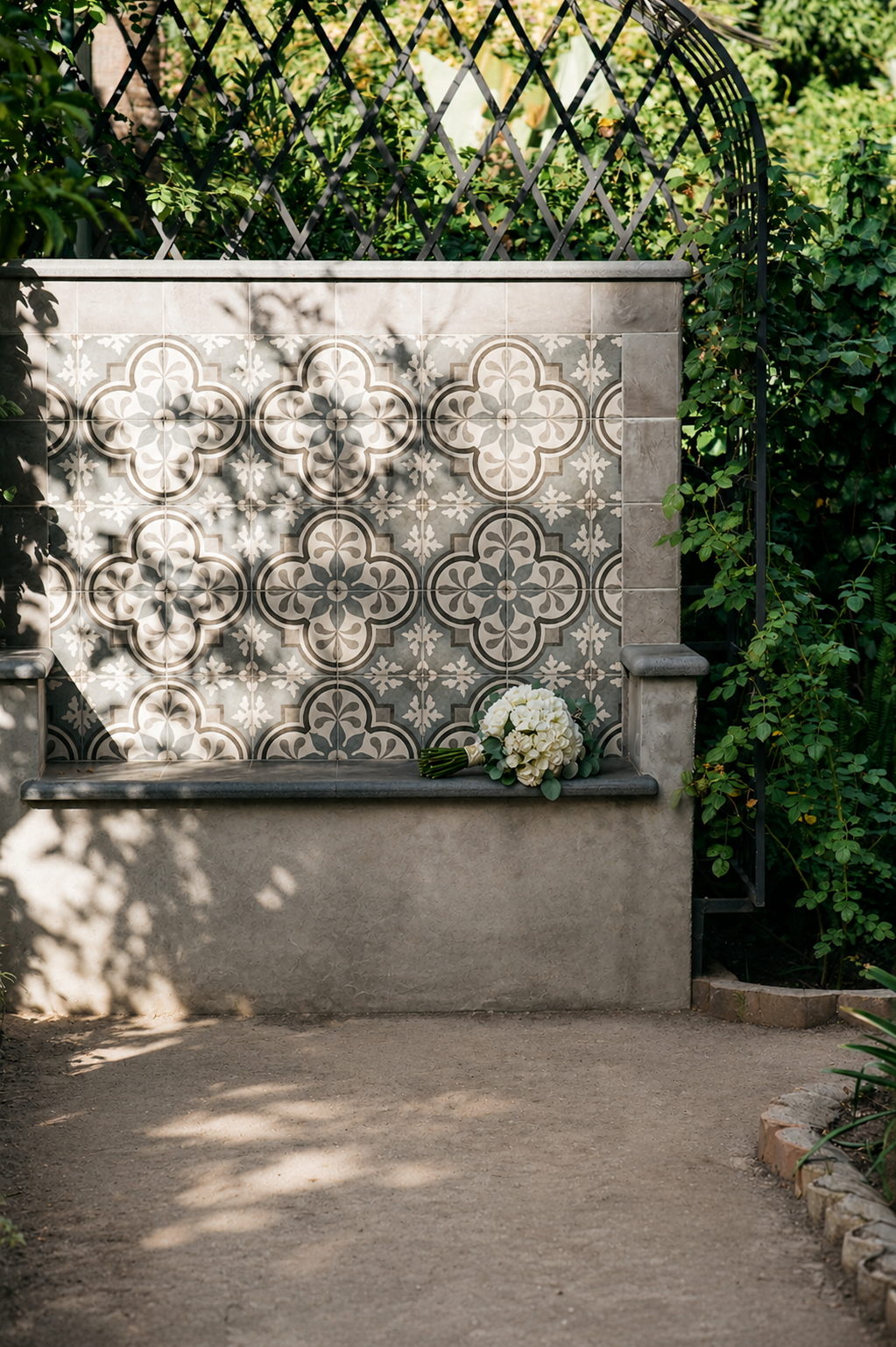 Gedenkmauer aus Stein mit gemusterten Fliesen und Blumen auf einem schattigen Gartenweg