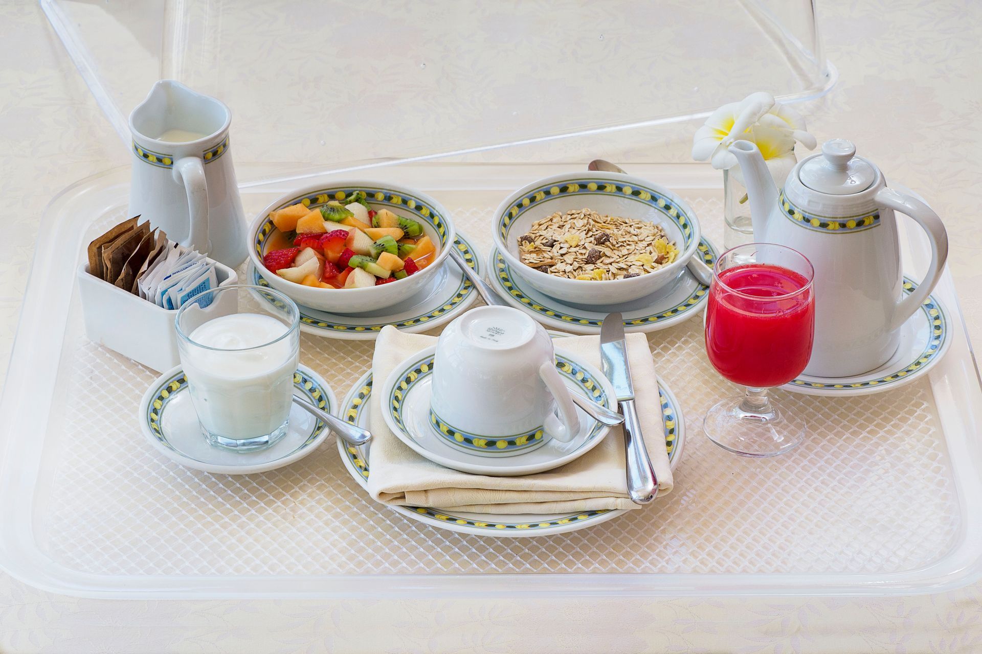 Elegantes Teeservice mit Tassen, Gebäck, Obst, Milch und rosa Saft auf einer weißen Tischdecke