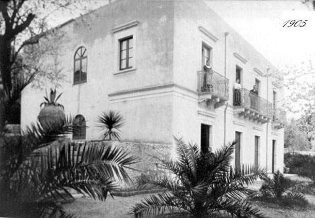 Photo en noir et blanc d'une maison de style méditerranéen à deux étages avec balcons et palmiers en façade