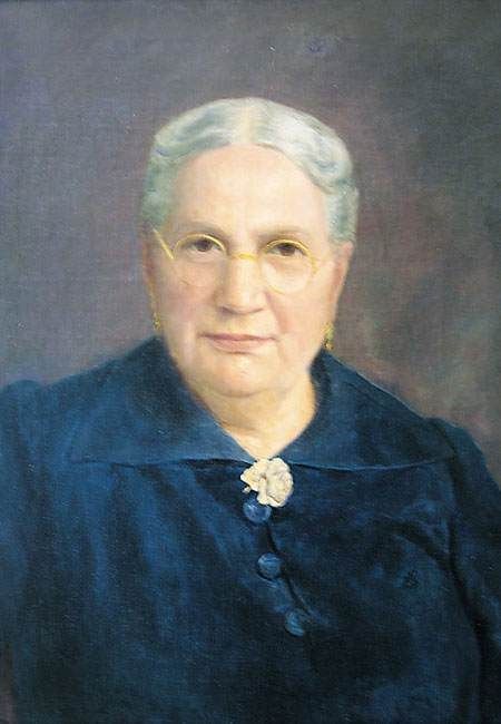 Portrait d'une femme âgée en robe bleu foncé, aux cheveux blancs et à l'expression neutre.