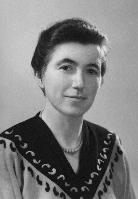 Portrait en noir et blanc d'une personne portant un pull à motifs et un collier, regardant l'objectif avec un léger sourire.