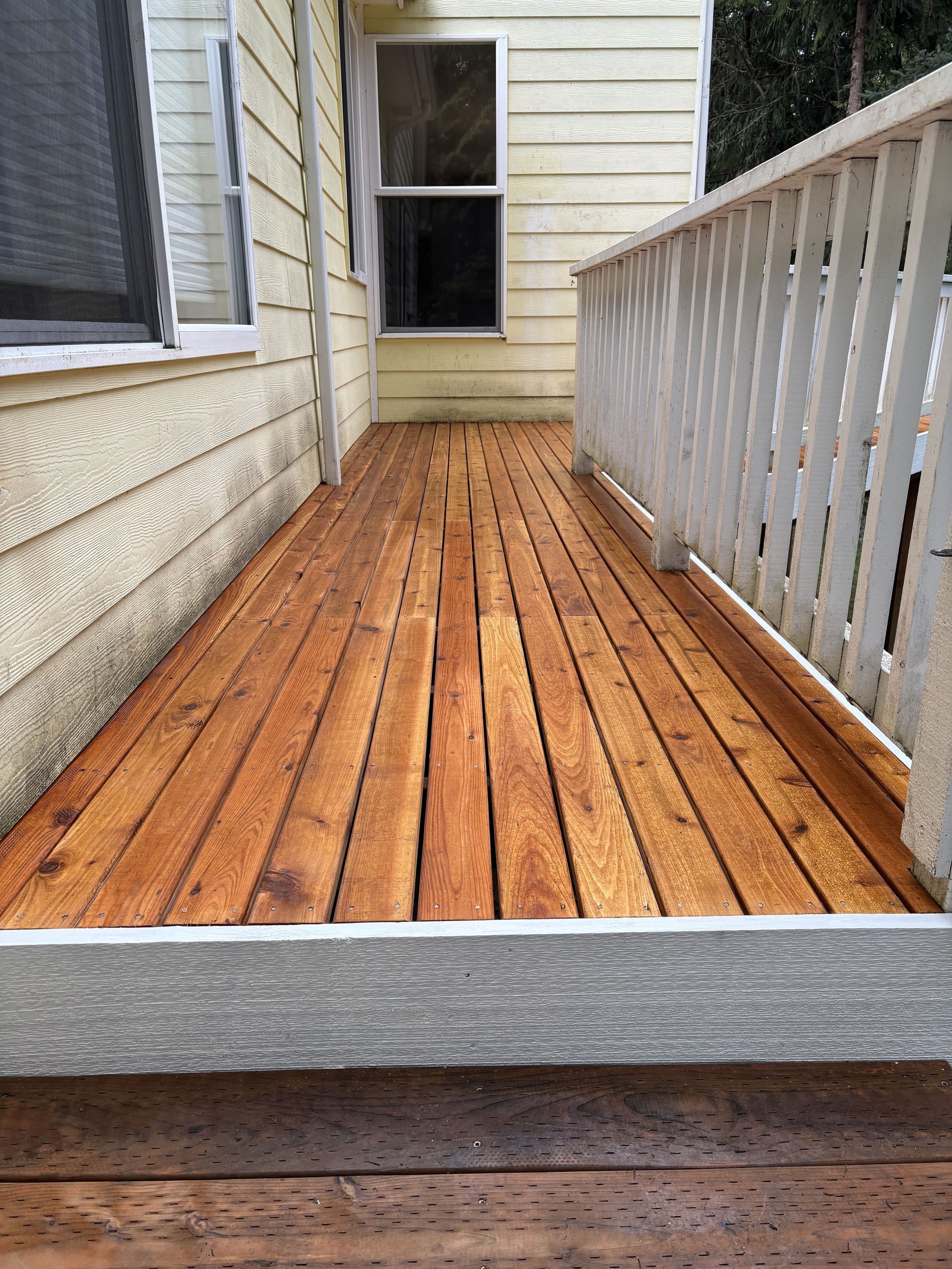 A wooden deck next to a house with a white railing.