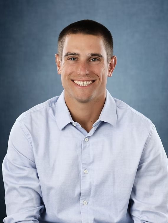 Man in light blue shirt smiles at the camera, against a blue background.