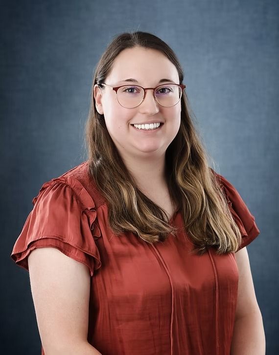 Woman with glasses and a red blouse smiles at the camera against a blue background.