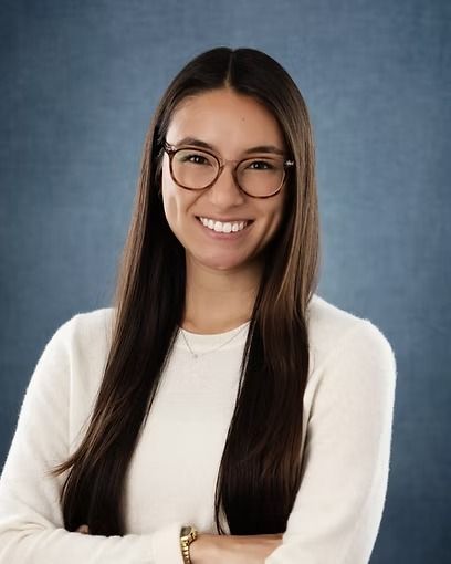 Woman with glasses, smiling with arms crossed, wearing a white sweater against a blue background.