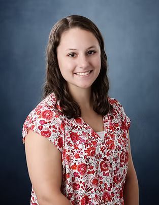 Woman in floral top smiles, posing in front of a blue backdrop.