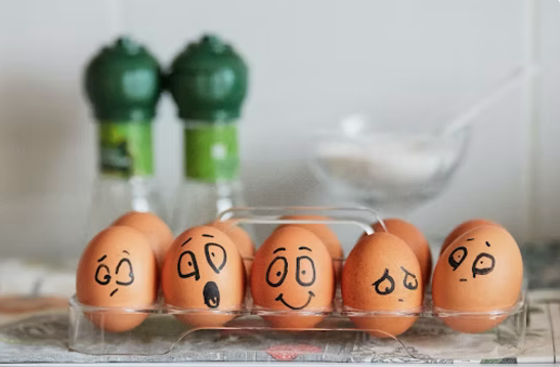 Eggs with drawn-on faces in a carton, salt and pepper shakers in background, showing various expressions.
