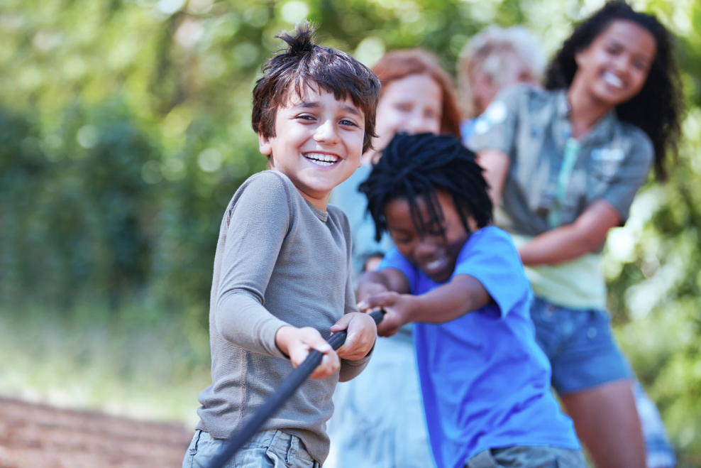 Children playing tug-of-war outdoors, smiling and laughing.