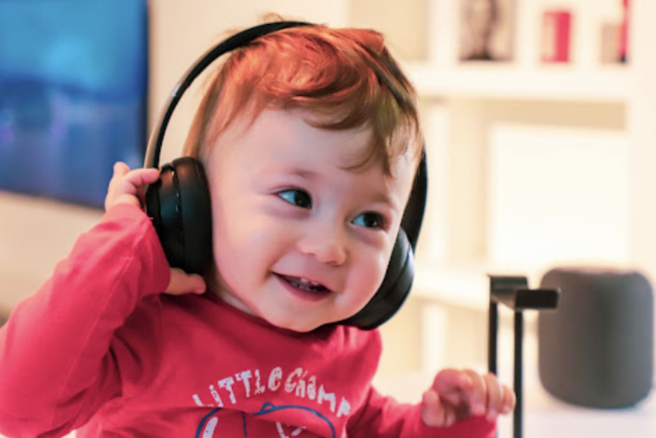 Smiling baby wearing black headphones, in a red shirt.