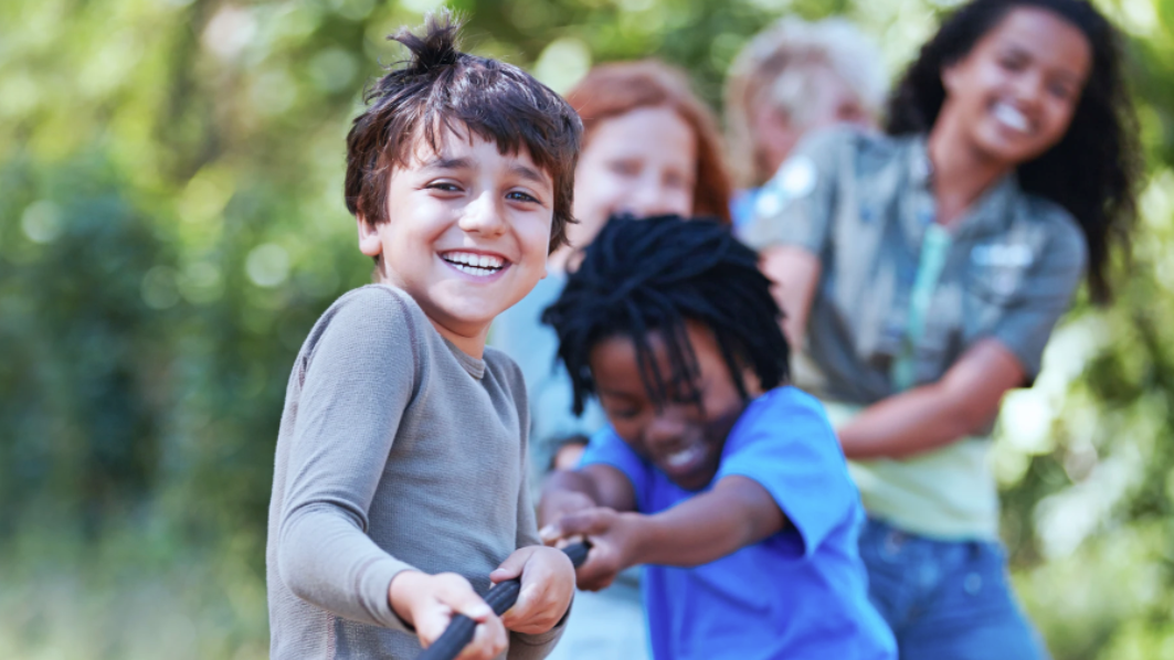 Children playing tug-of-war outdoors, smiling and laughing while pulling on a rope.