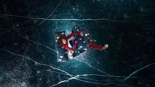 Person wrapped in a blanket on an ice surface, surrounded by cracks.