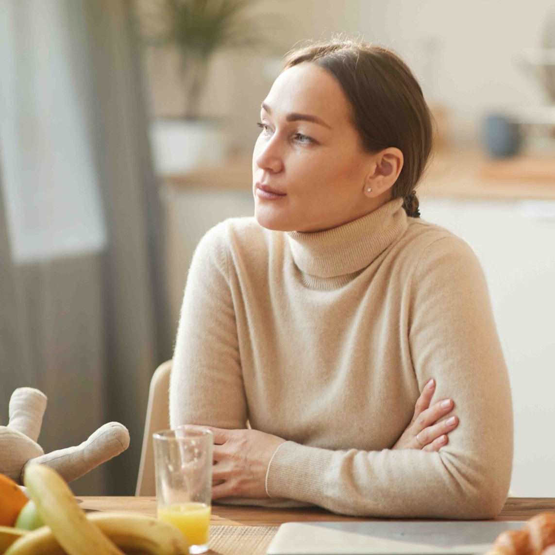 Woman with crossed arms, gazing away from a table with fruit and a glass of juice.