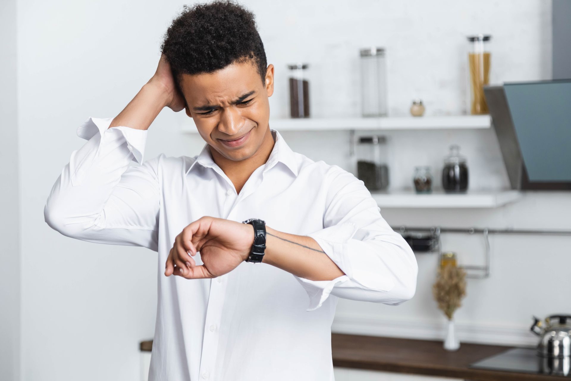 Man in white shirt looking at watch, appears stressed, in a kitchen.