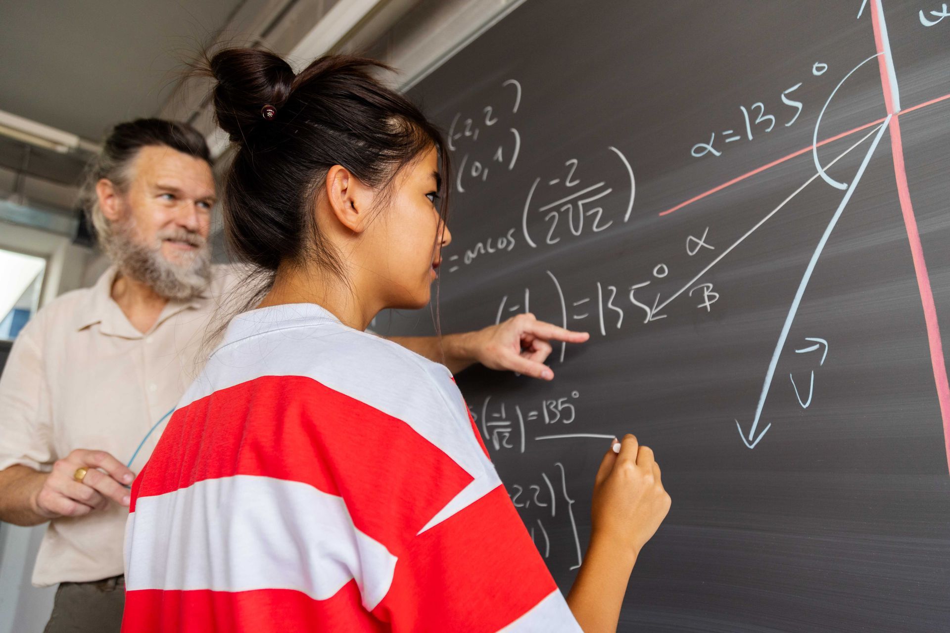 Student and instructor working on math problem on chalkboard.